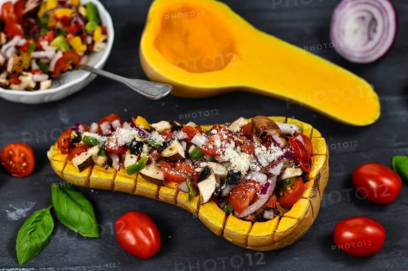 Vegan baked Butternut squash filled bell pepper, cherry tomatoes, red onion and mushrooms surrounded by ingredients on dark background