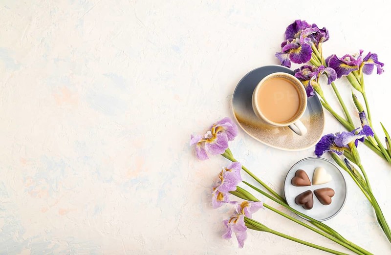 Cup of cioffee with chocolate candies and lilac iris flowers on white concrete background. top view, flat lay, copy space, still life. Breakfast, morning, spring concept