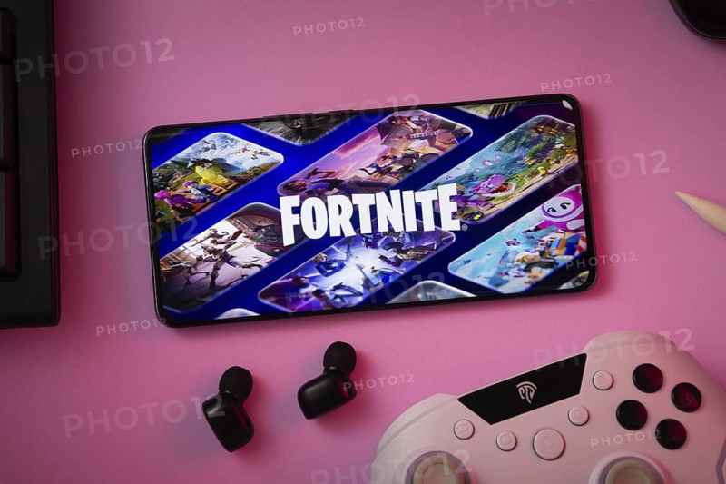 Dhaka, Bangladesh- 12 June 2025: Phone displaying Fortnite on pink surface with a gaming controller and earbuds