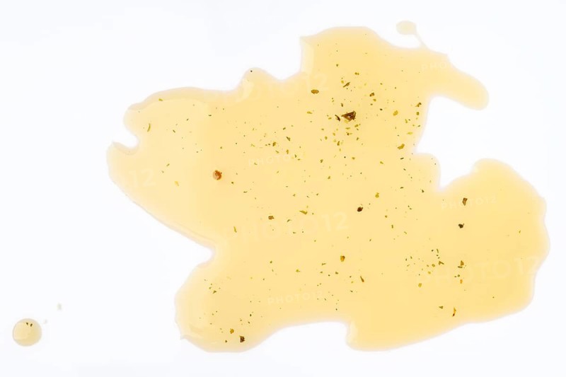 Spilled Olive oil with herbs with specks on a white background showcasing intriguing textures and colors