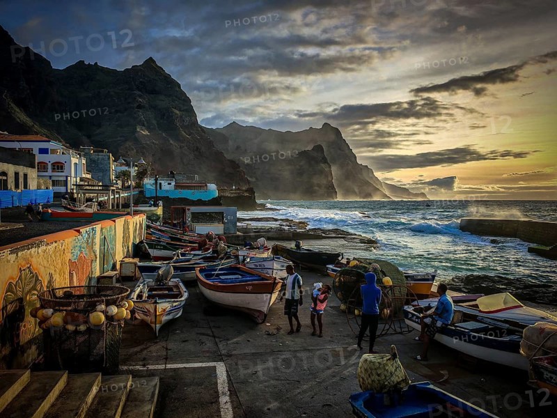 Four people at the harbor in front of dramatic light fishing net and colorful boats on the coast with an artistic wall, mural, graffiti and quiet evening mood at the fishing port, romantic, sunset, Ponta do Sol, Santo Antao, Cabo Verde, Cape Verde, Cape Verde