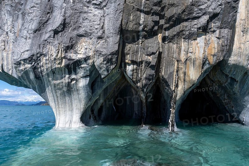 Marble caves (Capillas de Mármol) with striped rock formations over turquoise-coloured water, snow-covered Andes in the background, Lago General Carrera, Región de Aysén, Patagonia, Chile