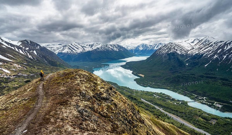 Climbers on a hiking trail on Slaughter Ridge, views of snowy mountains in spring and turquoise Lake Kenai Lake, Cooper Landing, Kenai Peninsula, Alaska, USA