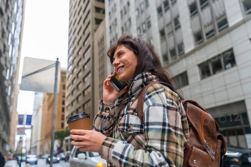 Young woman with backpack and takeout coffee walking downtown san francisco, smiling and talking on smartphone, energetic urban commuter enjoying a morning call