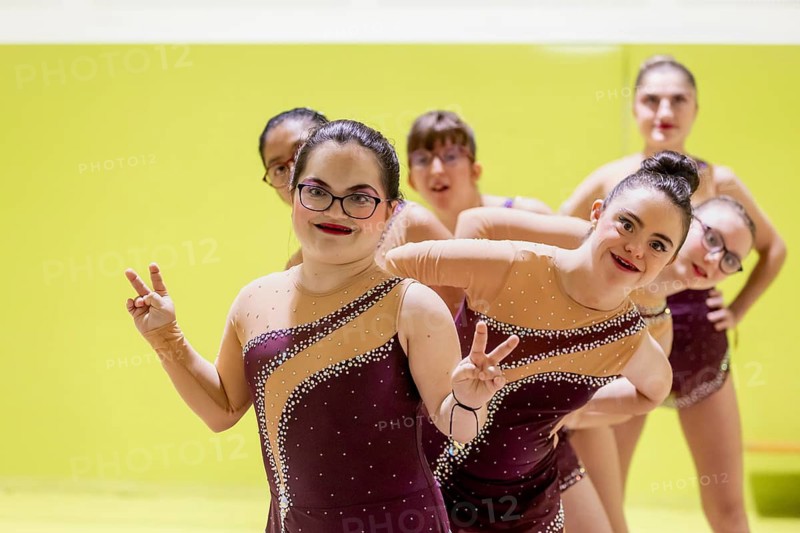 A joyful group of young disabled gymnasts in matching costumes express joy and camaraderie, highlighting unity and enthusiasm against a vibrant yellow background