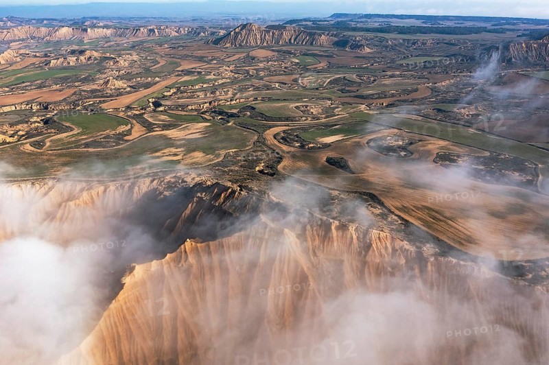 A stunning aerial view reveals a craggy landscape interspersed with lush fields Mist cloaks the terrain, adding a mysterious touch to the undulating scenery