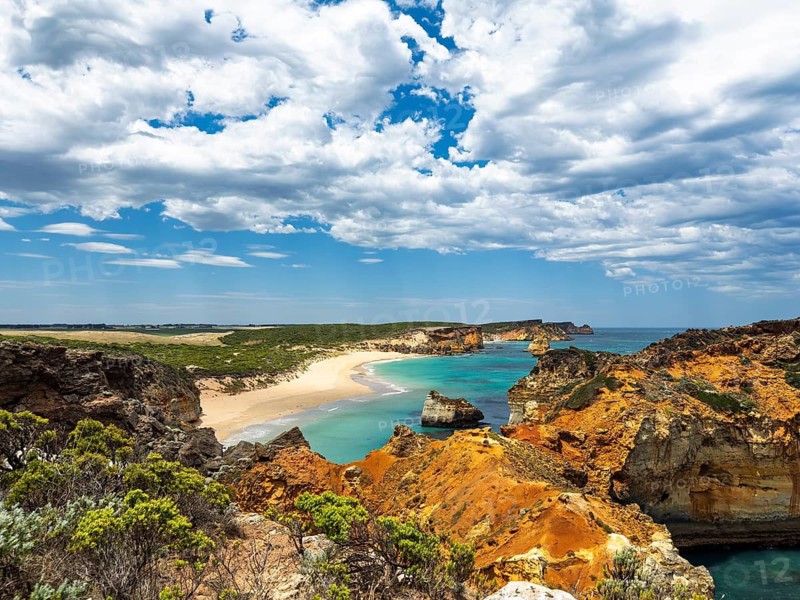 A breathtaking coastal scene showcases rugged cliffs, sandy beaches, and clear turquoise waters under a sky filled with dramatic clouds in the Twelve Apostles, Australia