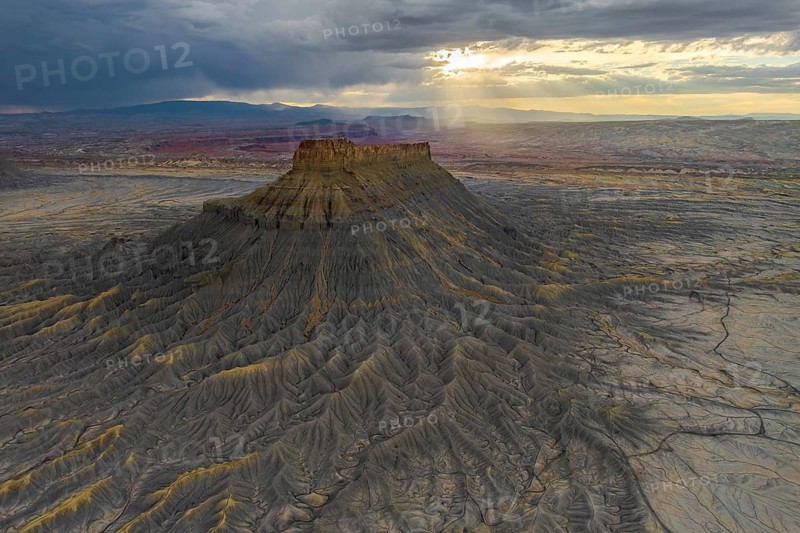 A dramatic view of Factory Butte as the sunset casts golden highlights across its rugged terrain, set against a vast desert landscape in Utah, USA