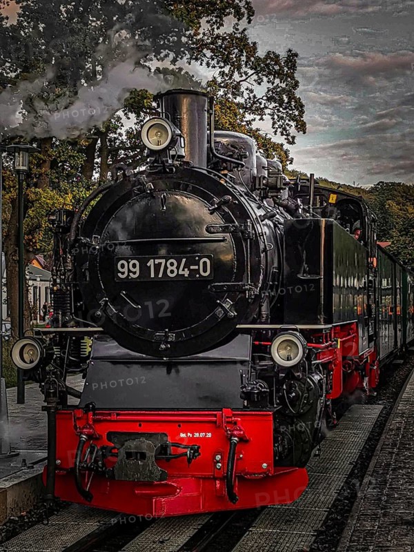 Old, historic steam locomotive in bright colors on tracks at the station in a nostalgic atmosphere, front view of speeding Roland on Rügen