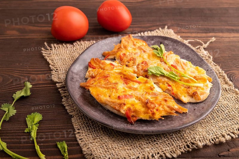 Baked chicken meat with cheese and tomatoes on brown wooden background and linen textile. side view, close up