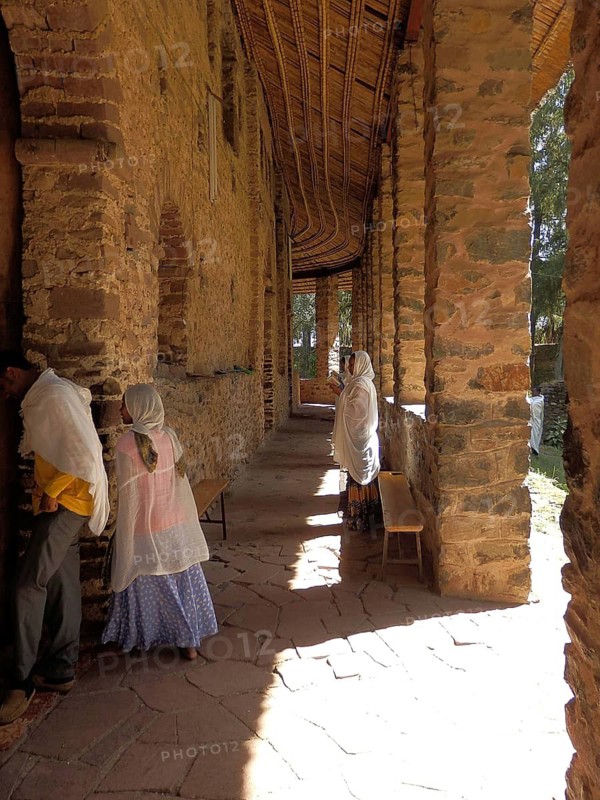 Sunlit corridor with traditionally dressed people and stone walls, Debre Birhan Selassie Church, Fasil Ghebbi, Historic Stone Building, Orthodox Church, Gondar, Ethiopia
