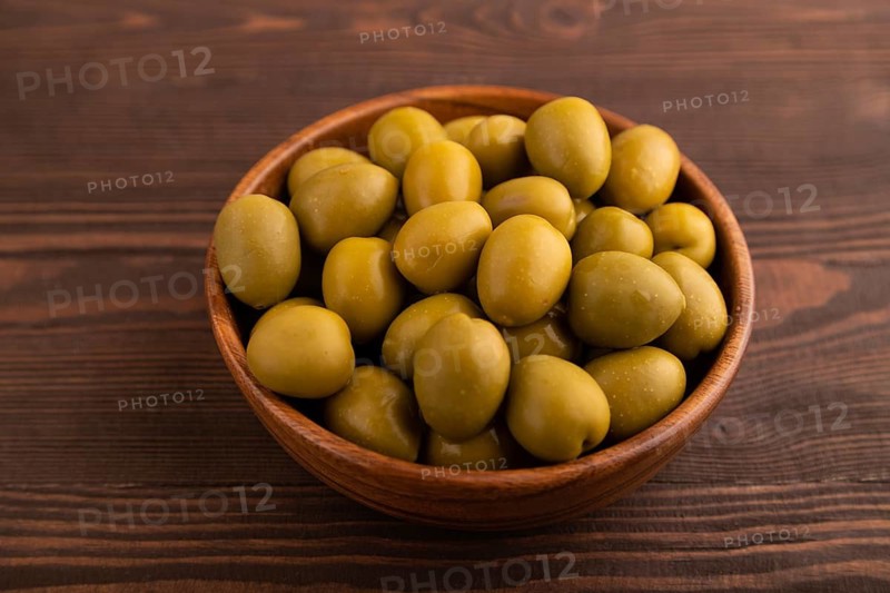 Fresh green olives in wooden bowl on brown wooden background. side view, close up