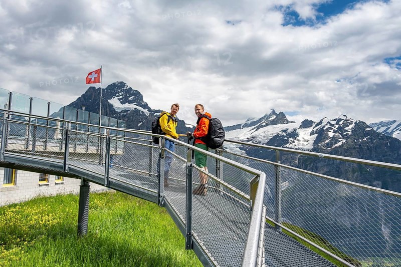 Tourists on the First Cliff Walk, metal trail on a rocky outcrop, Grindelwald First, in front of impressive mountain landscape with Schreckhorn summit and Upper Grindelwald glacier, Bernese Alps, Bernese Oberland, Switzerland