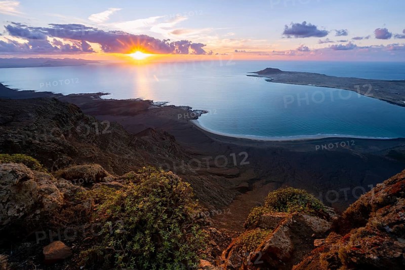 View from steep cliffs to sea and coast with sun stars, Mirador del Porrito viewpoint at sunset, Lanzarote, Canary Islands, Spain