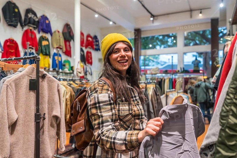 Young woman smiling in a trendy san francisco thrift shop, holding a vintage garment while enjoying sustainable fashion, browsing unique second hand finds and expressing style
