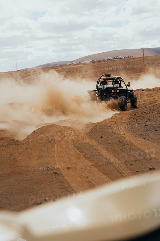 A thrilling off-road vehicle navigating the dusty, rugged terrain of Lanzarote, with rolling hills and a cloudy sky creating a dramatic backdrop for adventure