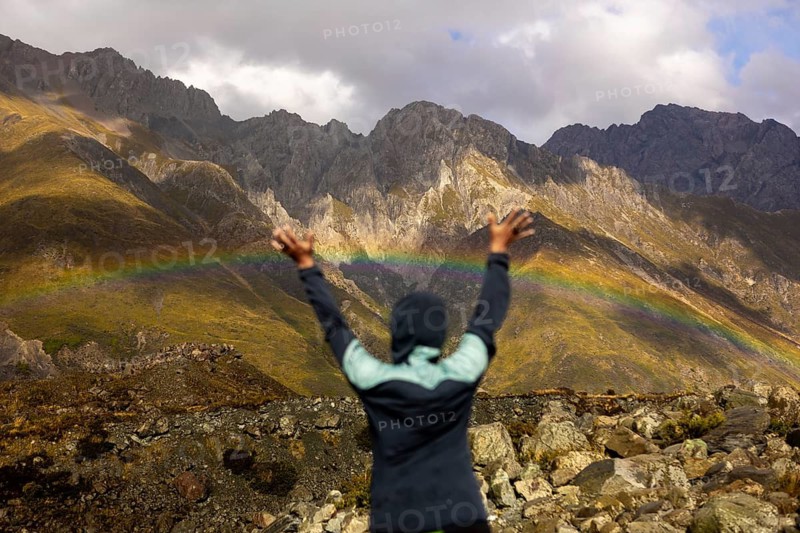 A woman wearing a jacket raises her arms in joy, surrounded by the stunning autumn landscape of Mount Cook, New Zealand, with rocky terrain and majestic peaks