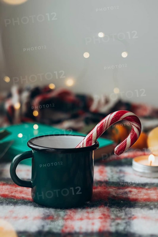 Green mug with a steaming beverage and a classic candy cane, set against a festive, softly lit background, conveying the warmth and cheer of the holiday season