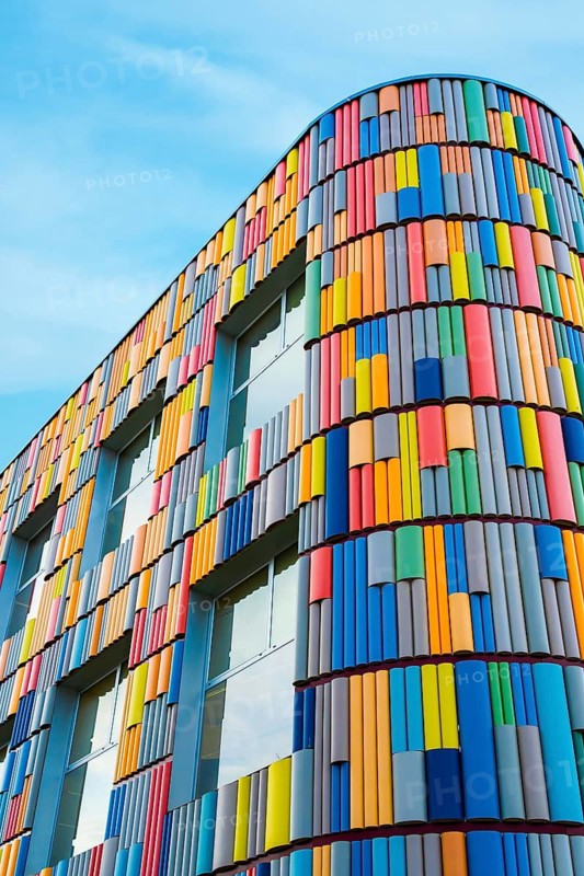 A modern building featuring a vibrant, multicolored, curved facade against a clear blue sky captures attention with its playful design and architectural beauty