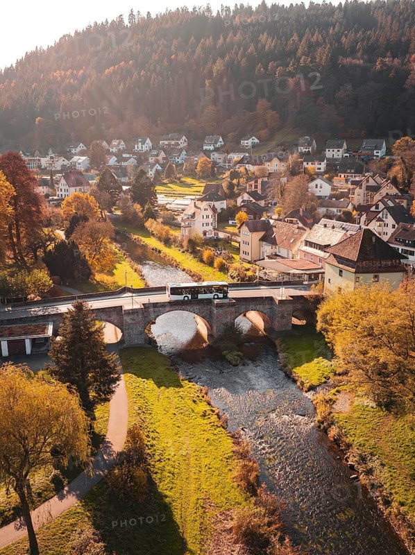 Village with river and bridge in a picturesque autumn landscape surrounded by hills, Calw, Black Forest, Germany