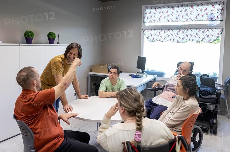 A group of individuals engage in activities at a day center for people with mental disabilities, fostering community and interaction. The room is bright and welcoming