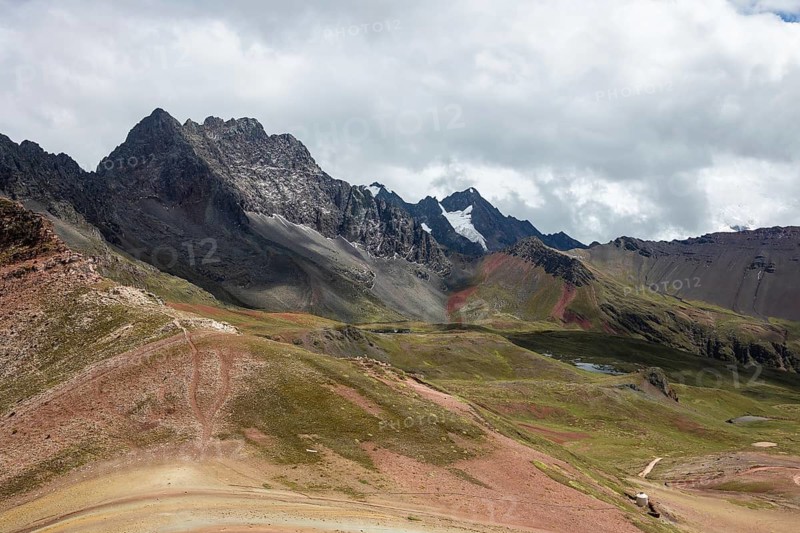 A breathtaking panoramic view of the rugged, multicolored landscape of the Rainbow Mountains in Peru, showcasing rocky peaks under a cloudy sky