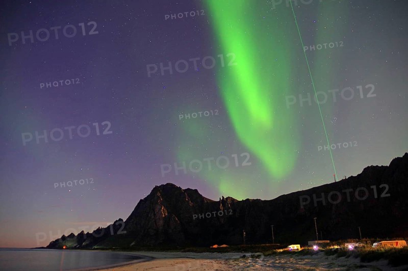 Northern lights glow over a rocky coastline with beach and illuminated areas at night, Laser, Andøya Space, Bleik, Vesteralen, Norway