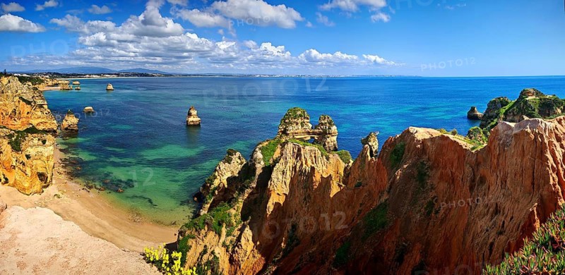 Panoramic view of a rocky coastal landscape, beach, lush green vegetation with clear blue sea and sky, Ponta da Piedade, Lagos, Algarve, Portugal