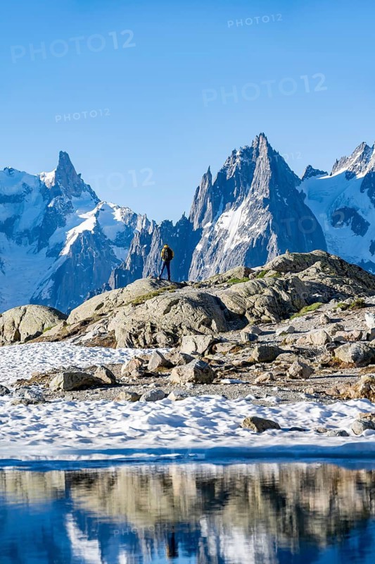 Young man in front of impressive mountain landscape in morning light, reflection in the Lac Blanc mountain lake, mountain summit, Aiguille Verte, Grandes Jorasses, Aiguille du Moine, Mont Blanc, Mont Blanc Massif, Chamonix-Mont-Blanc, Haute-Savoie, France