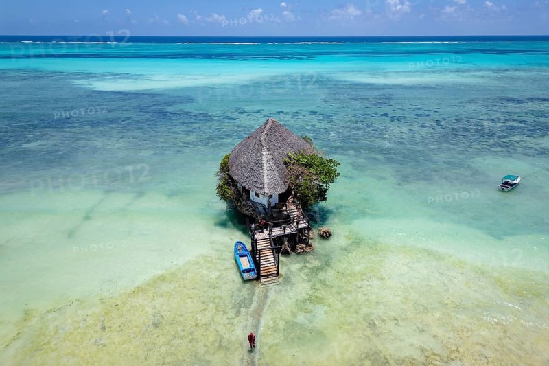 Aerial view of the building surrounded by turquoise water and white sand beach with boats under a clear blue sky in Zanzibar