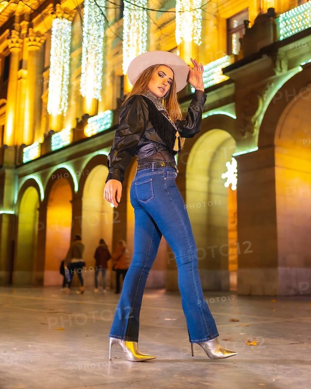 Winter lifestyle, young caucasian blonde model wearing jeans and a black jacket in the city illuminated for christmas at night