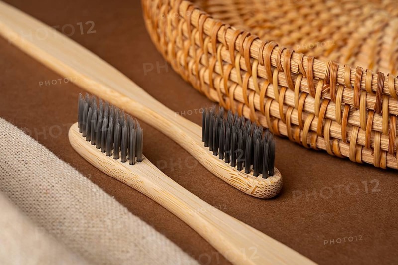 From above view showcasing bamboo toothbrushes with black bristles on a brown surface paired with a woven basket and beige fabric, creating an eco-friendly aesthetic
