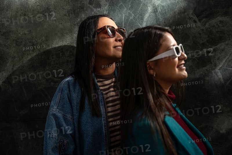 A Latin lesbian couple wearing stylish sunglasses, basking in a joyful moment together. Their trendy outfits and serene expressions highlight love and connection