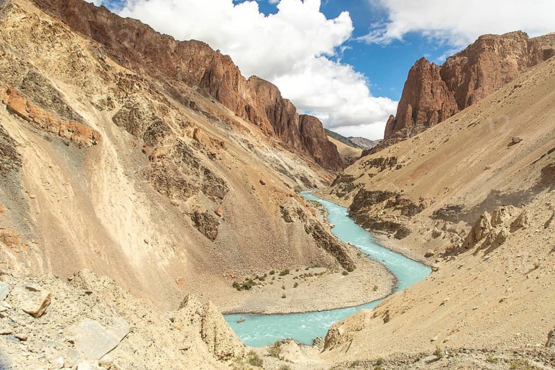 A stunning landscape of a turquoise river winding through rugged mountains in Ladakh. The arid terrain and bright sky enhance the natural beauty of this remote region in India