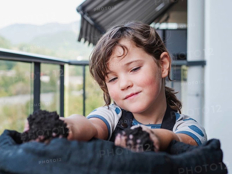 A young girl holds rich garden soil in her hands while playing outdoors, showcasing early education in gardening