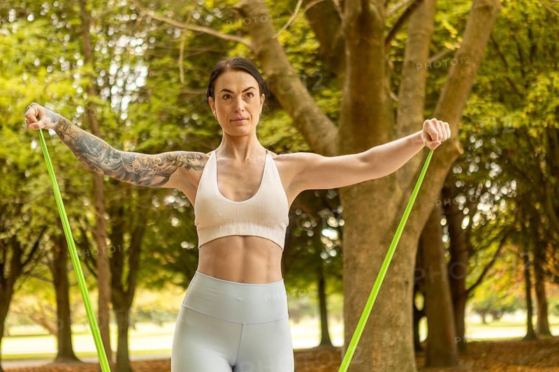 A woman exercises with resistance bands in an autumn New Zealand park, surrounded by trees. Her focus is evident as she enjoys an invigorating outdoor workout session