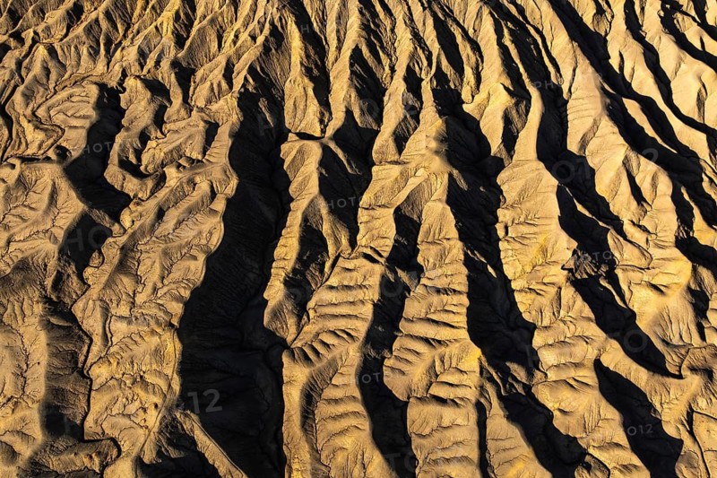 Aerial view of golden desert textures at Caineville Mesa, Utah. Features notable ridges and shadows, enhancing the unique geological formations and patterns