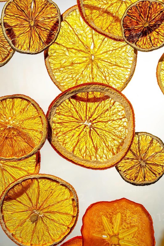 Vibrant display of dried citrus fruit slices including oranges and lemons, backlit to enhance their translucent, colorful textures