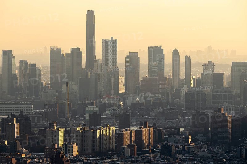 Top view of New York City's skyline enveloped in a hazy glow as the sunsets, highlighting the contours of skyscrapers and residential buildings