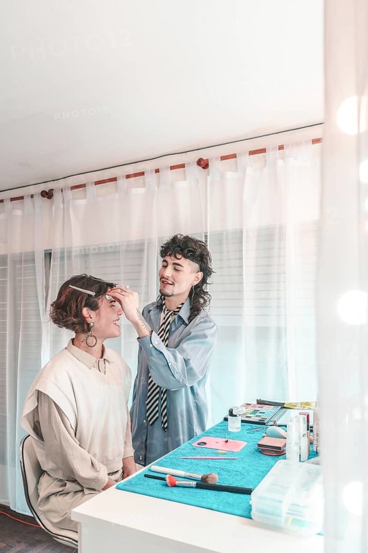 Professional makeup artist carefully applying makeup on a model's face, preparing her for a photoshoot or event in a bright studio setting, showcasing diversity and inclusion in the beauty industry