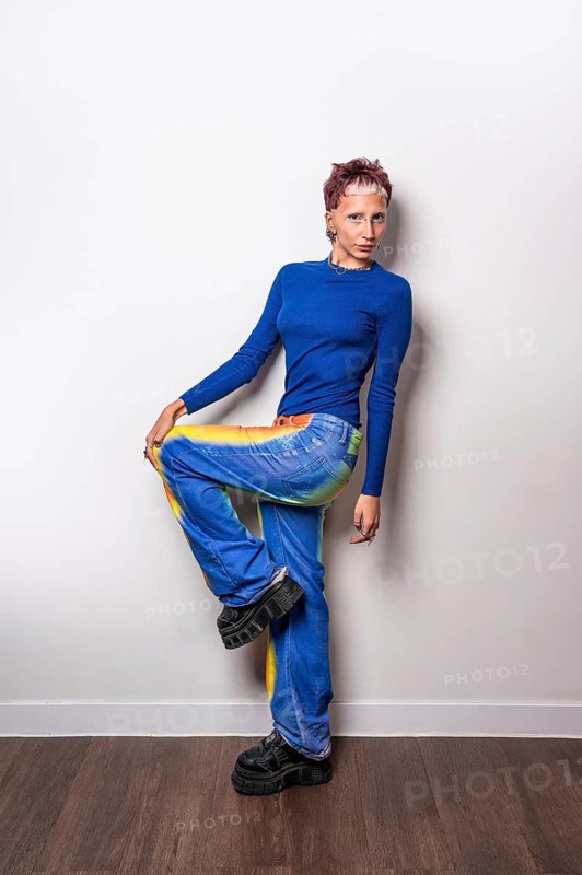A fashionable young woman poses confidently in trendy, brightly colored trousers and a blue top, exuding modern, artistic style. Perfect for contemporary fashion concepts
