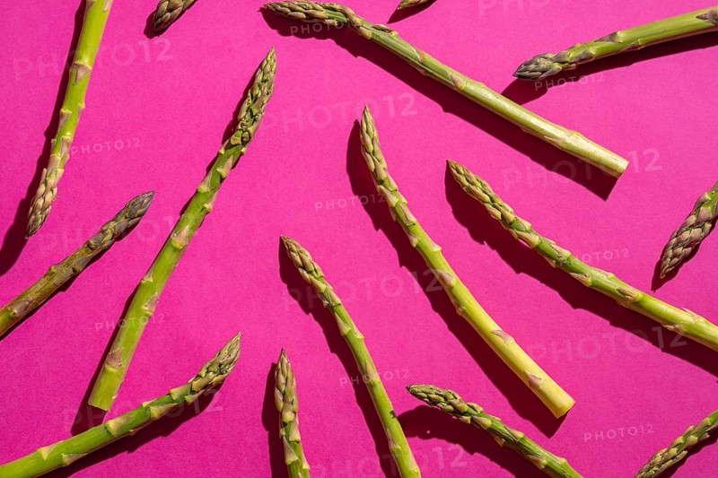 Fresh asparagus spears are artfully arranged on a vibrant pink background, creating a striking contrast. The fresh green hues highlight their natural appeal and culinary potential