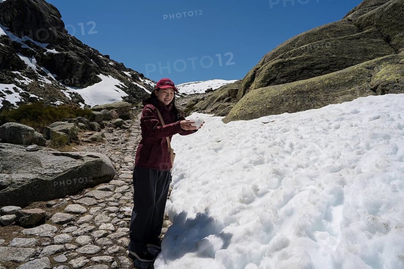 An Asian woman explores the stunning Sierra de Gredos in Spain, embraced by snow-capped mountains and clear blue skies, epitomizing a moment of travel and adventure