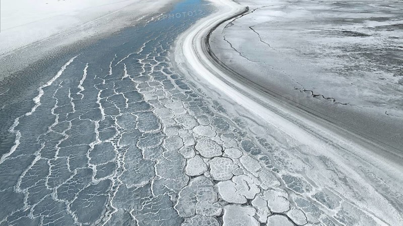 An aerial view of saline mud creates intricate textures and patterns on a vast surface, highlighting the natural beauty of an arid landscape with cracked layers and earthy tones