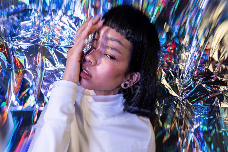 A futuristic Latin woman poses in a metaverse-inspired environment, surrounded by vibrant, iridescent colors, capturing the essence of virtual reality and digital culture