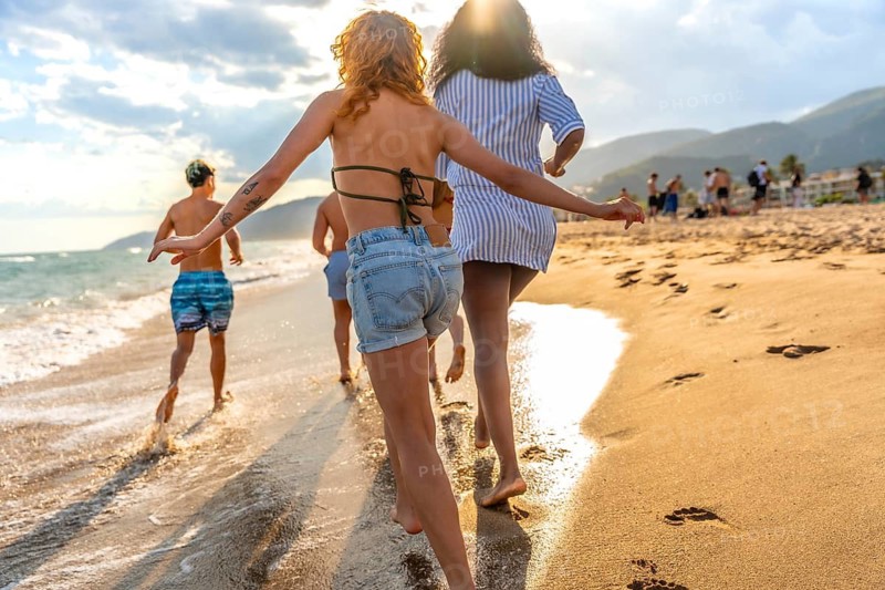 Group of friends running joyfully along the beach at sunset, savoring their summer vacation and the beauty of the ocean waves