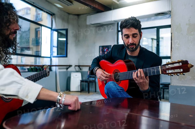 Male friends playing guitars at table in music studio