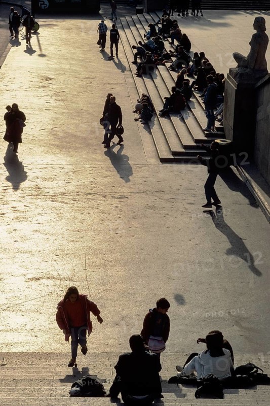 A group of people are walking along the street, some are sitting on the steps. The scene is casual and relaxed, people enjoying their time outdoors. Trocadero, Paris, France