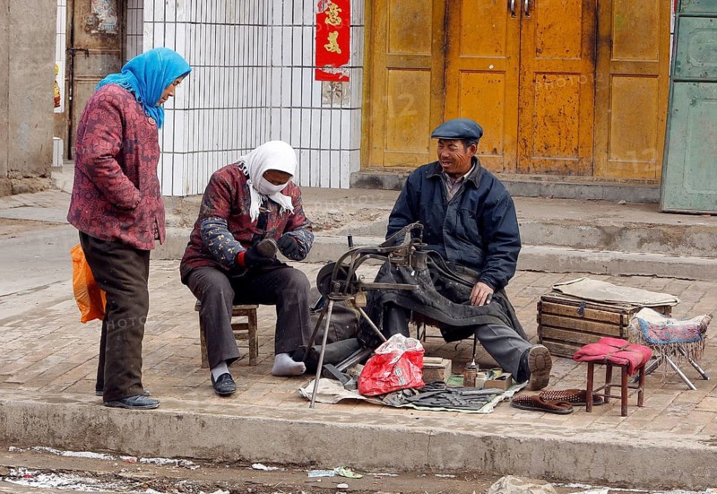 Xining, CHN, 27.02.09 - A woman puts on her repaired shoe at a shoemaker. A woman puts on a repaired shoe at a roadside cobbler in a village near Xining, CHINA