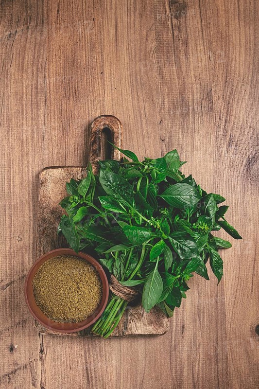 Ground green basil, in a ceramic bowl, with a bouquet of fresh green basil, on the table, top view, no people